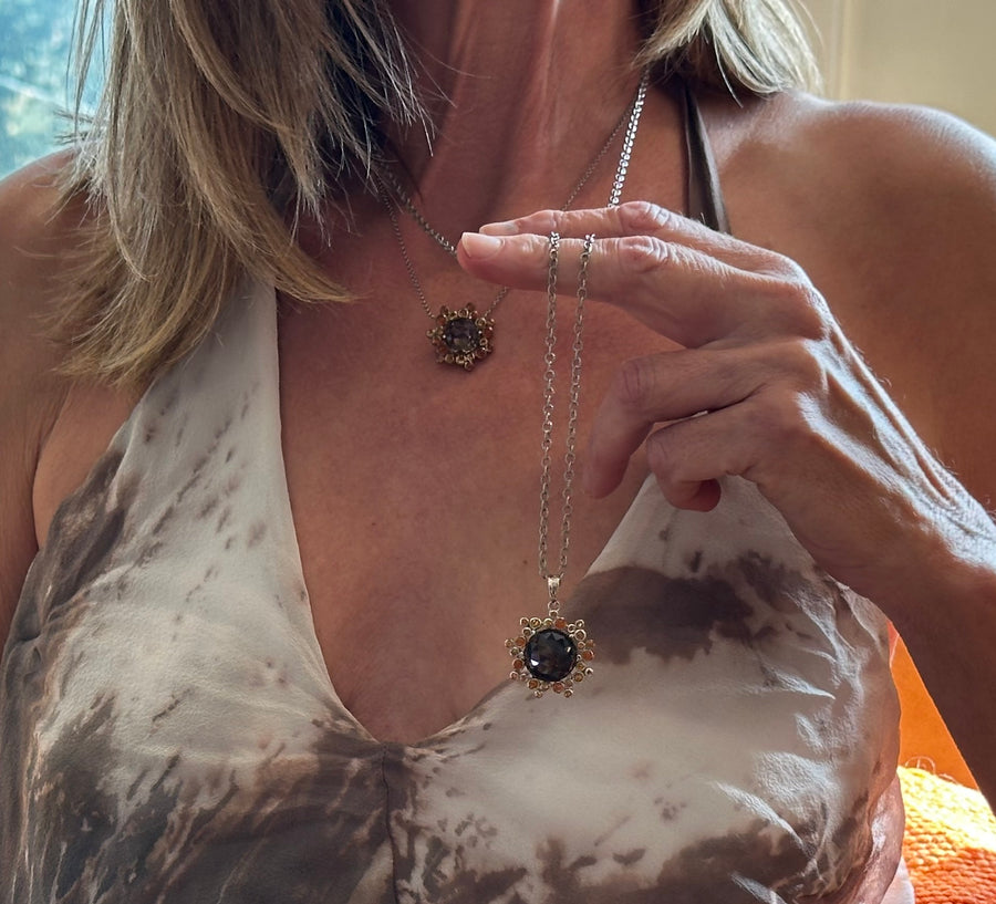 Photograph of a sterling silver necklace with a sunburst pendant featuring a large faceted smoky quartz stone encircled by smaller amber-colored gems