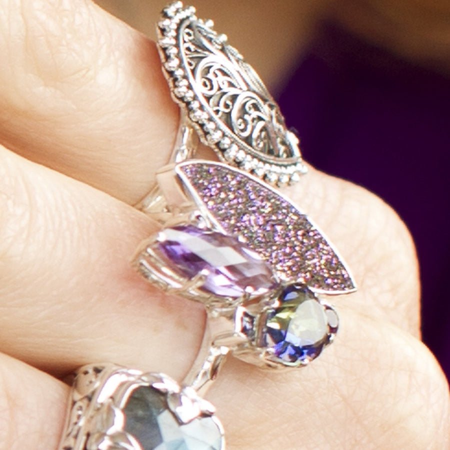 Photograph of a sterling silver cocktail ring with a marquise amethyst, iridescent mystic topaz, and sparkling deep purple druzy on a hammered band