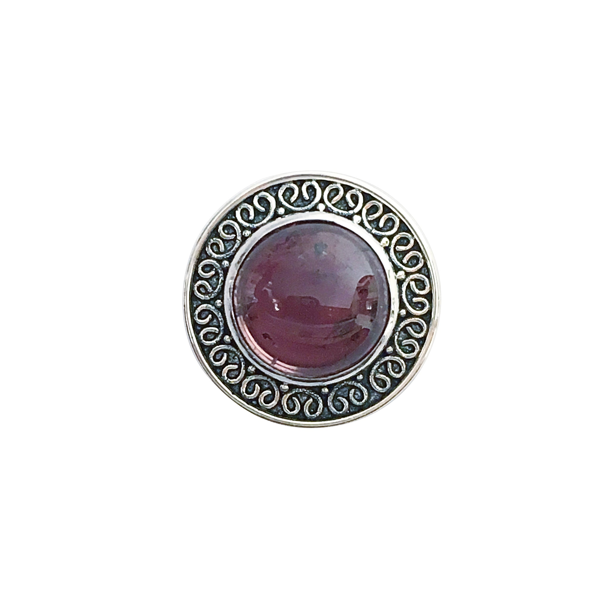 A round silver medallion featuring a central deep purple domed gemstone surrounded by intricate antique filigree scrollwork with dark oxidized details on a white background